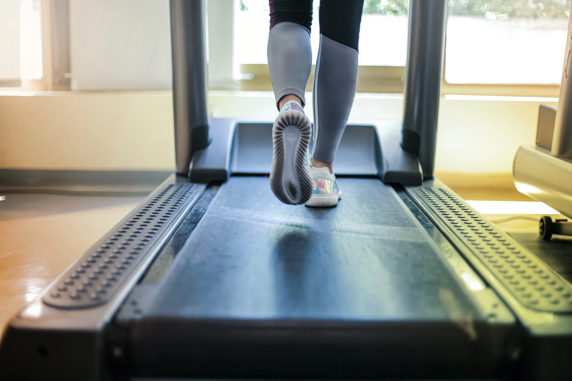 The view of a person's legs and shoes on a treadmill, depicting the core component of a cardiac stress test to monitor heart health during exercise.